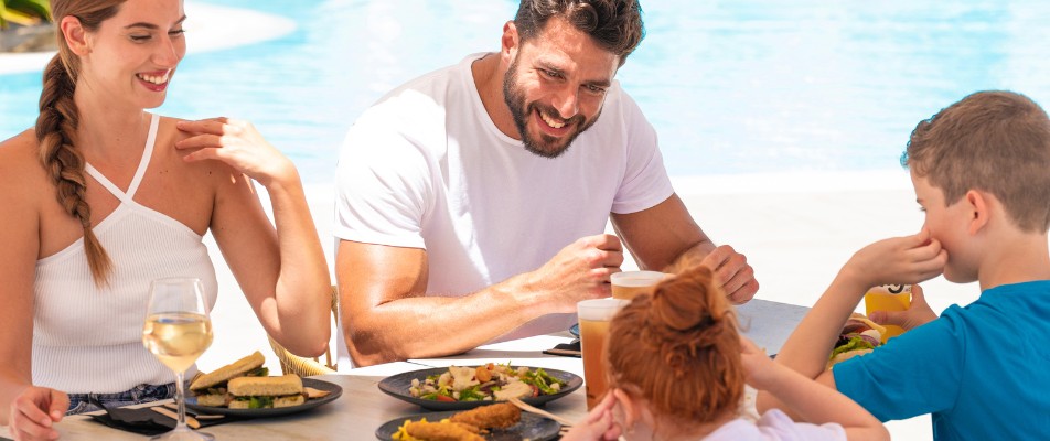 Familia disfrutando de una comida al aire libre junto a la piscina del hotel