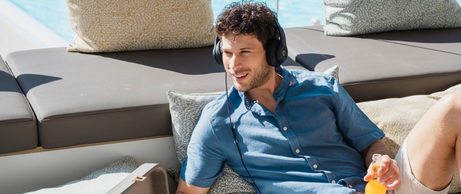 Hombre relajado con auriculares, un libro y una bebida en una tumbona al sol